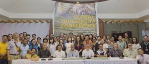A group of participants at the Global Indigeneity Conference standing and sitting behind a conference desk.