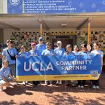 A group of UCLA student volunteers poses together on a brick courtyard under a covered walkway at Warner Avenue Elementary School.