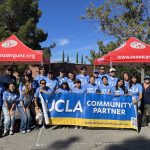 A group of UCLA student volunteers poses together outdoors under red event tents during the Sunland-Tujunga community tree planting event.